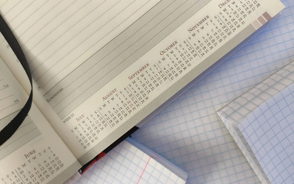 An open calendar planner resting on squared notebooks.