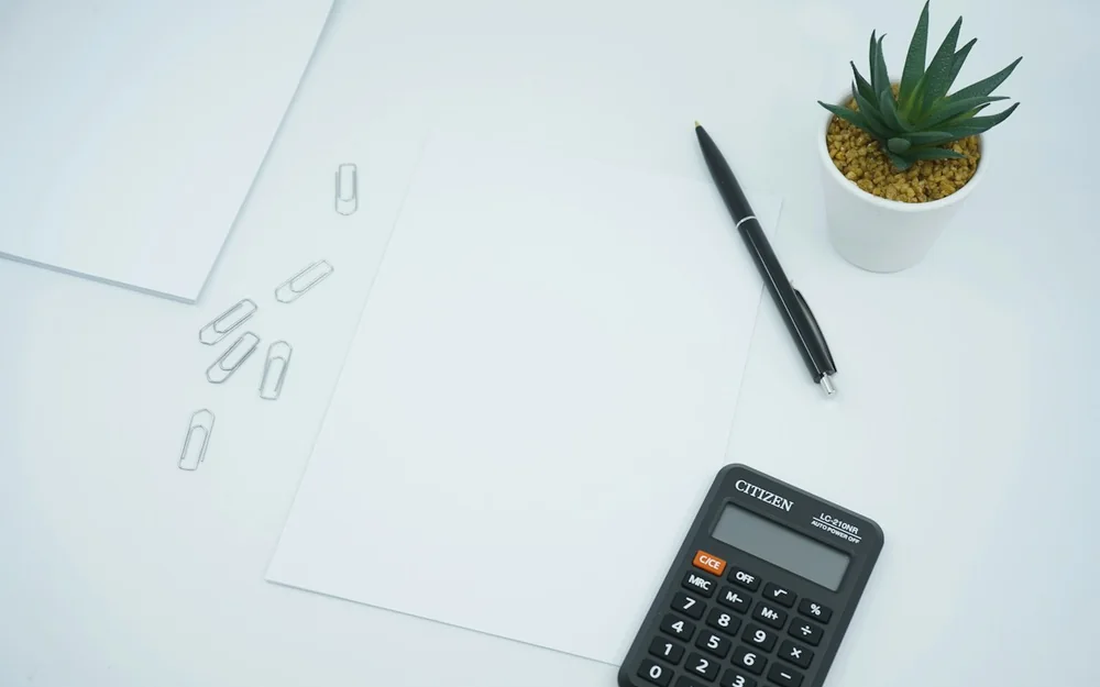A calculator, pen and blank papers on a pale desk.