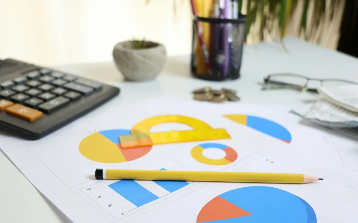 Printed financial charts beside a calculator, pencil and glasses.